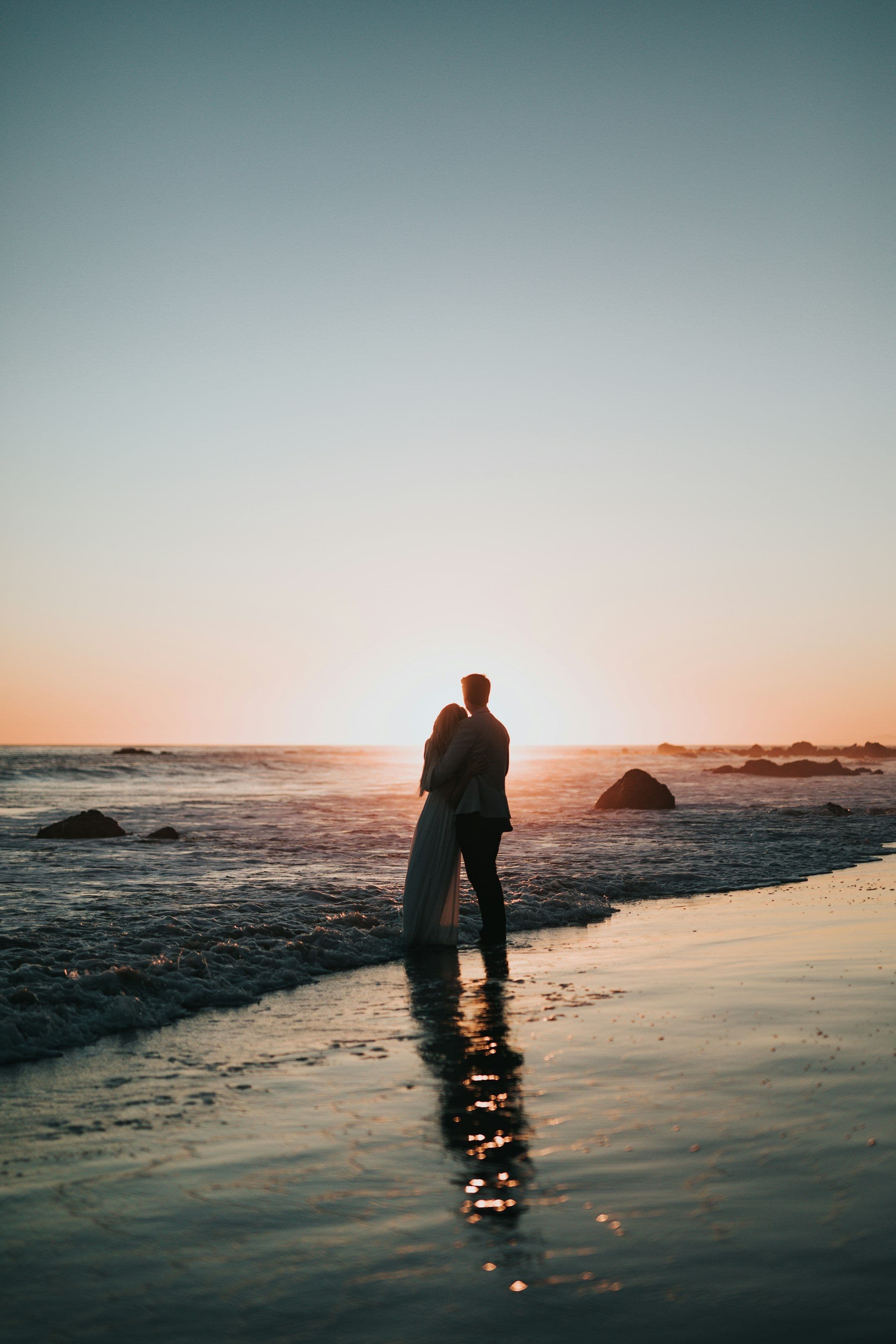 Casal em silhueta observando o pôr do sol na praia